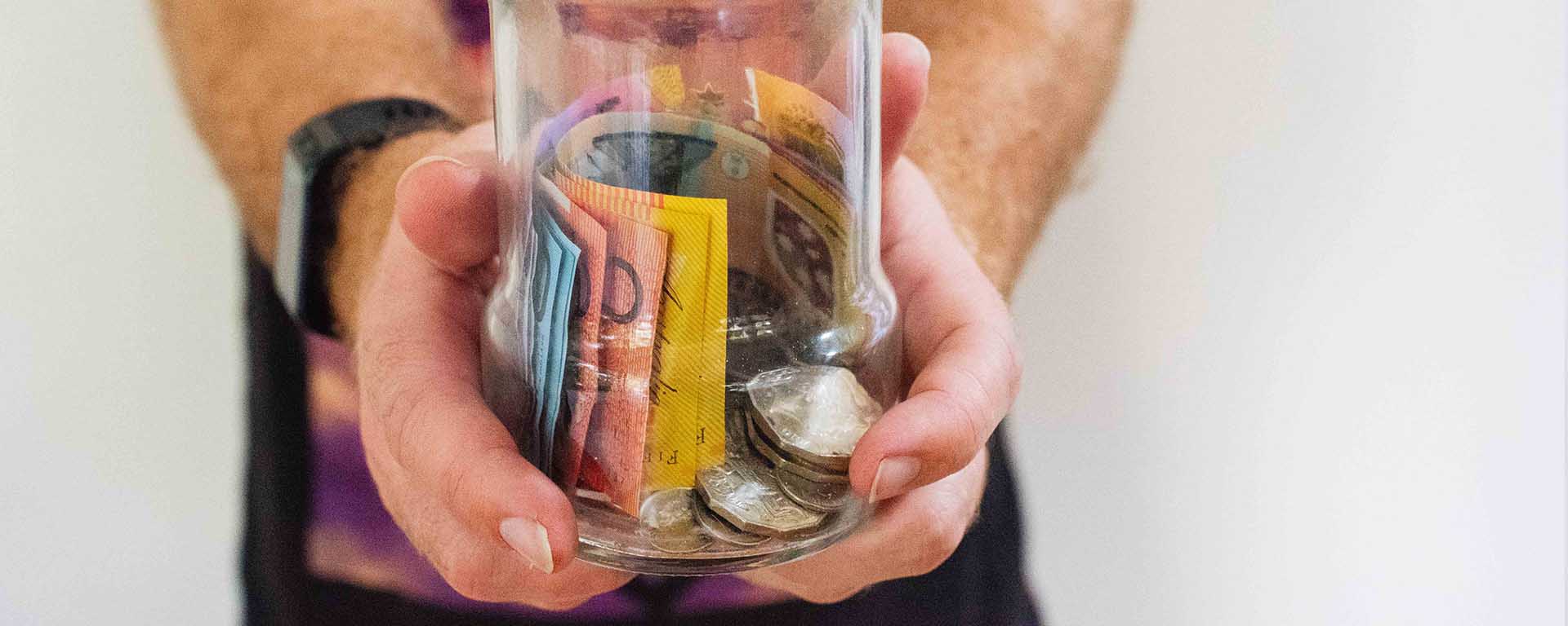A white man holds out a jar with money
