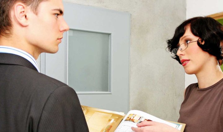 A white man frowns as a white woman is talking to him and pointing to a book