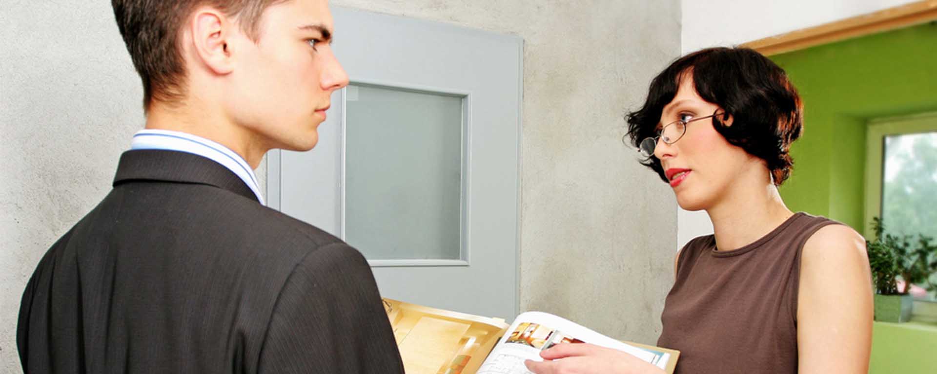 A white man frowns as a white woman is talking to him and pointing to a book