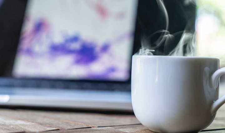 White mug with steam. A laptop in the background