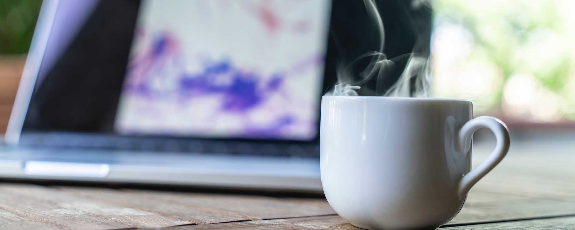 White mug with steam. A laptop in the background