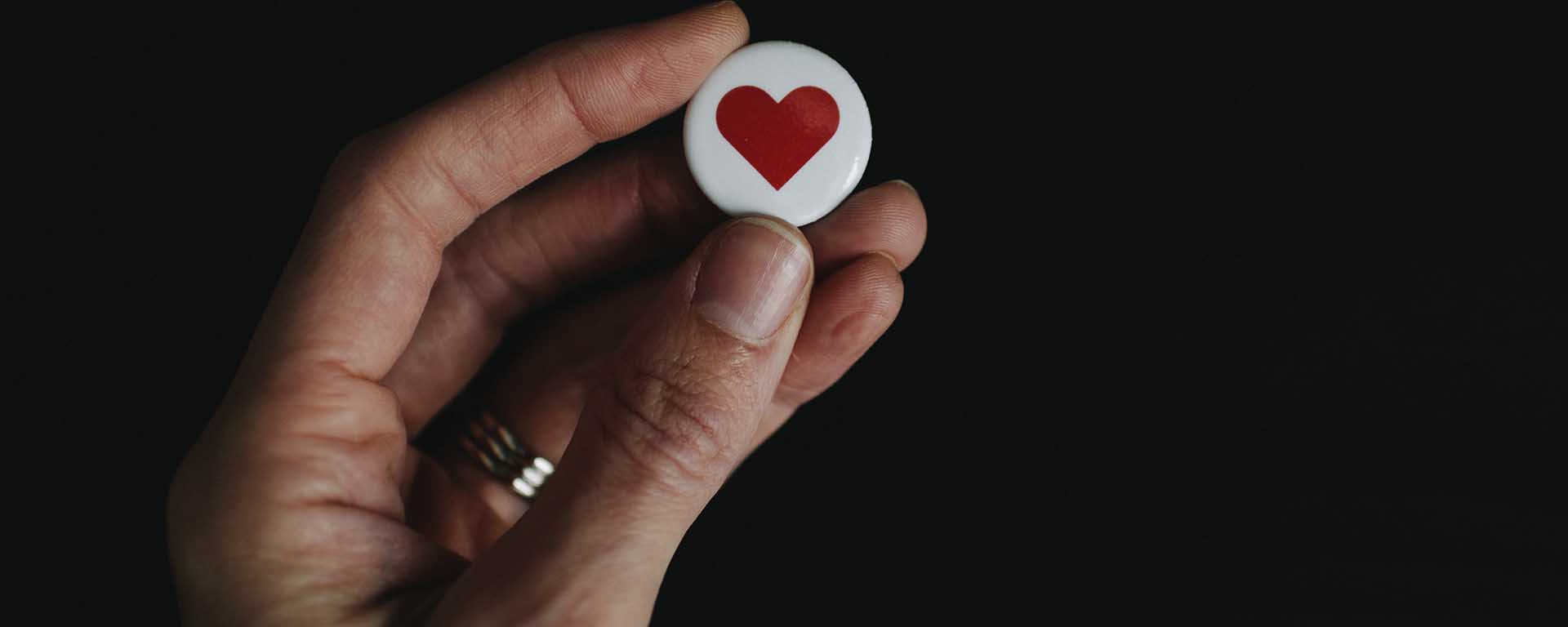 A hand holds up a white badge with a red love heart