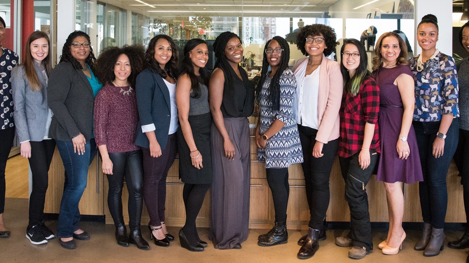 A dozen women are lined up in an office, smiling