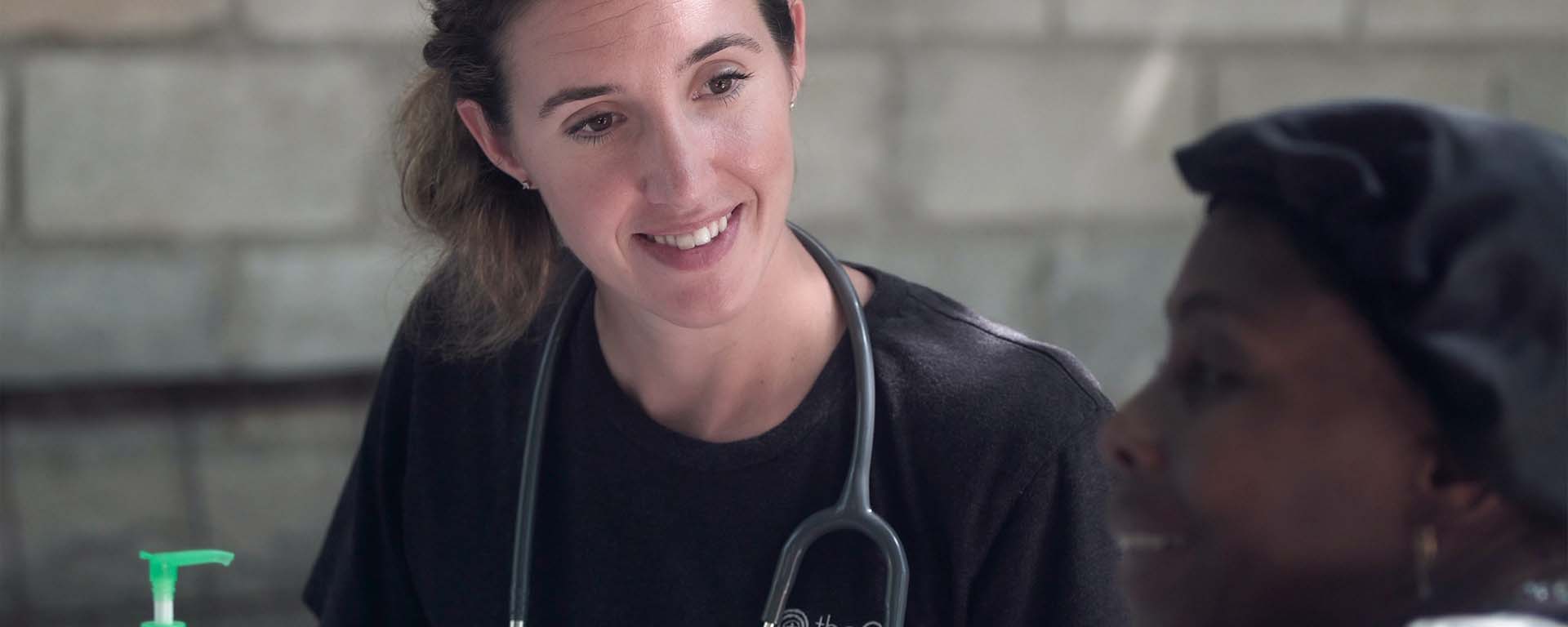 A white woman with a stethoscope smiles at a Black woman patient