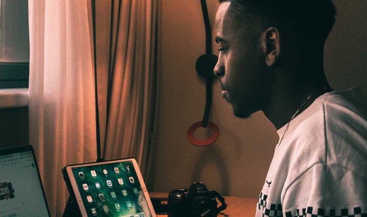A young Black man sits in front of a laptop