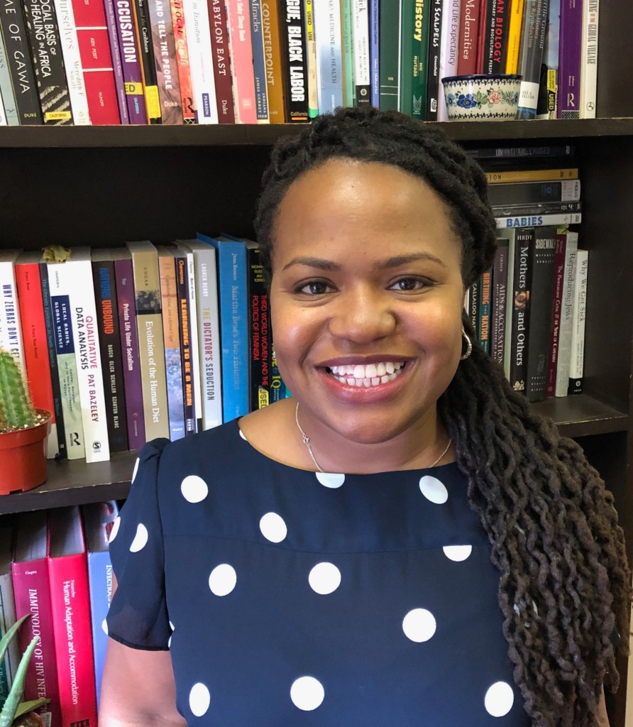 Dr Robin Nelson is a Black woman. She is smiling in front of a bookcase