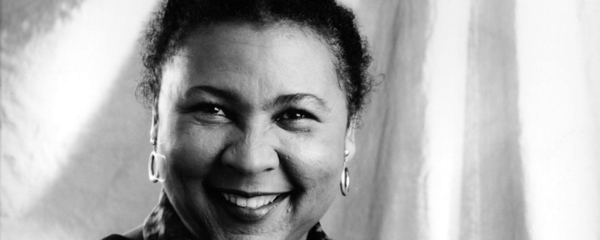 bell hooks is a Black woman. She is smiling, with her dark hair pulled back