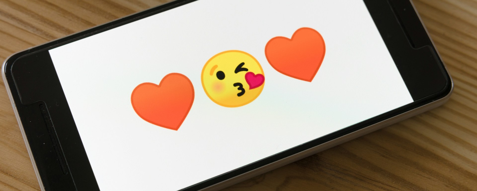 A phone showing two love hearts and a kiss emoji