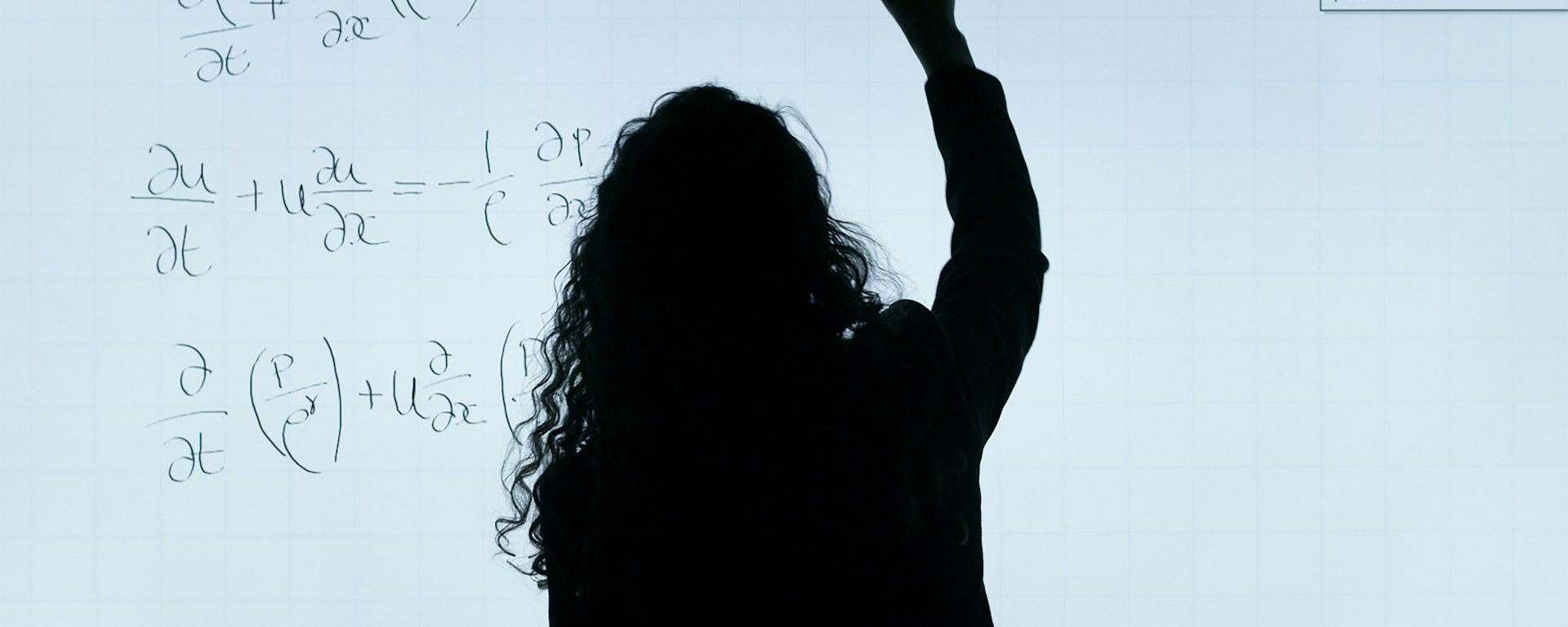 A woman with curly hair writes equations on a board