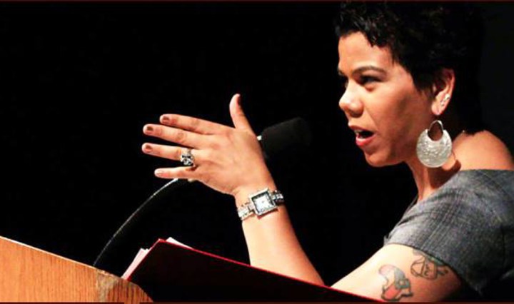 Rosa Clemente is a Black-Puerto Rican woman. She is standing at a podium pointing her hand forward as she speaks