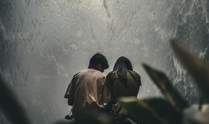 Two people sit with their back to the camera, in front of a large water wall