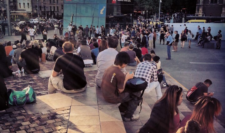 People sit on the Federation Square steps, in Melbourne