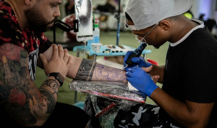 A man tattoos another man on the arm