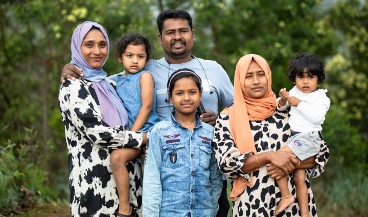 A family of one man, two women and three children stand together and smile