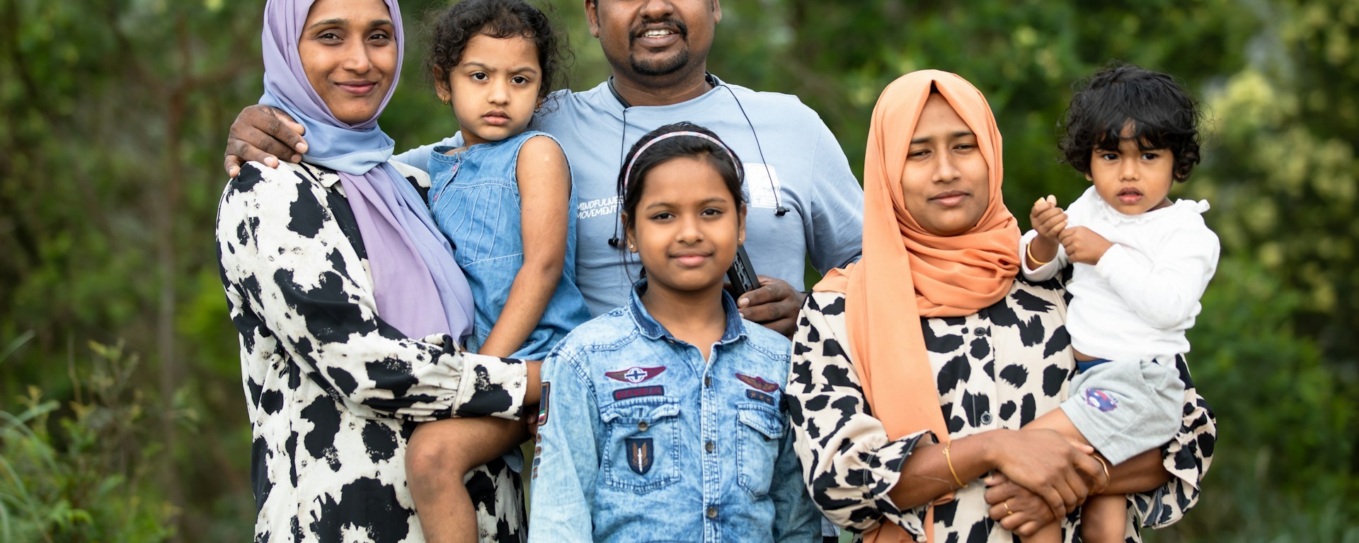A family of one man, two women and three children stand together and smile