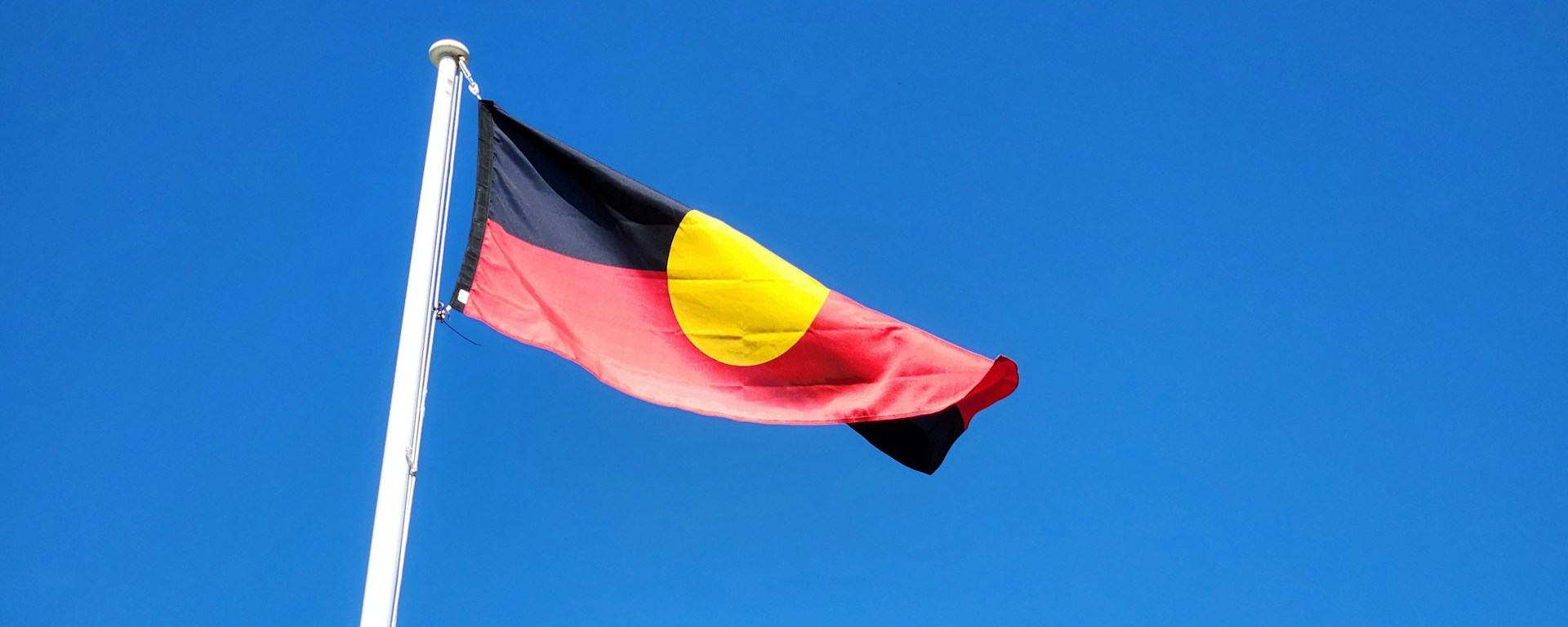 Aboriginal flag flies high against a blue sky