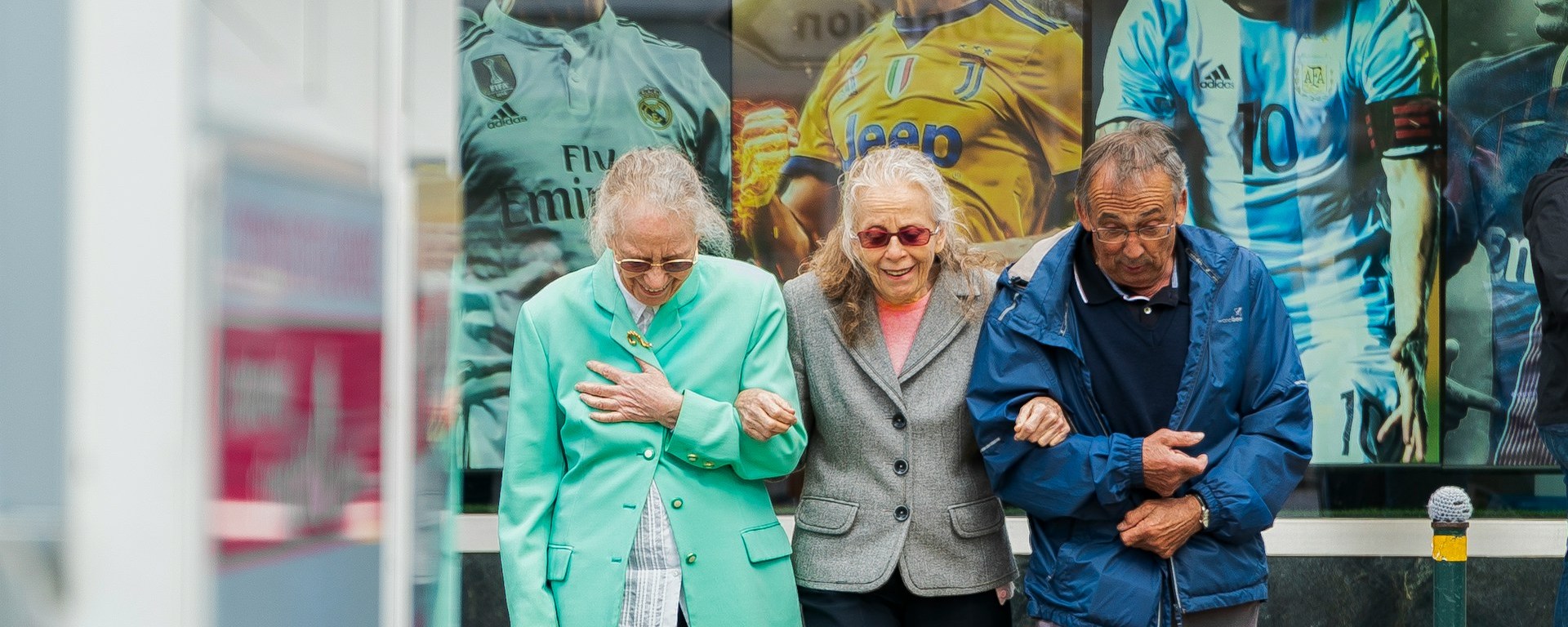 Two older women and one man are walking down the street, with their arms interlocked