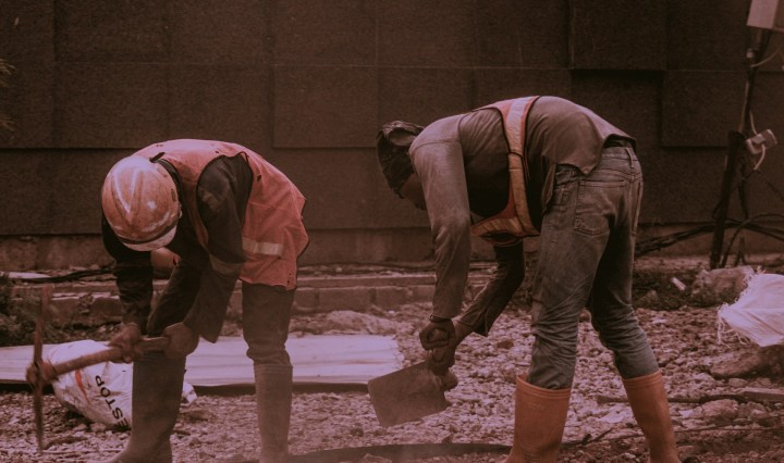 Two bricklayers work bent over