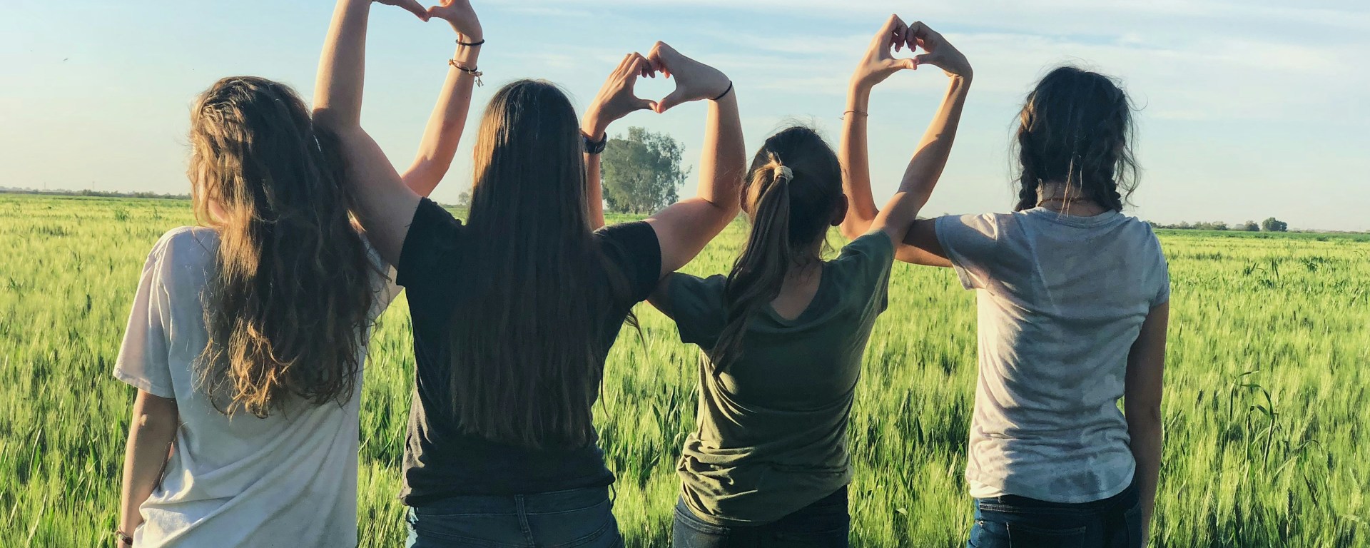 Girls sit with their back to the camera, with interlocking hands to make a heart sign