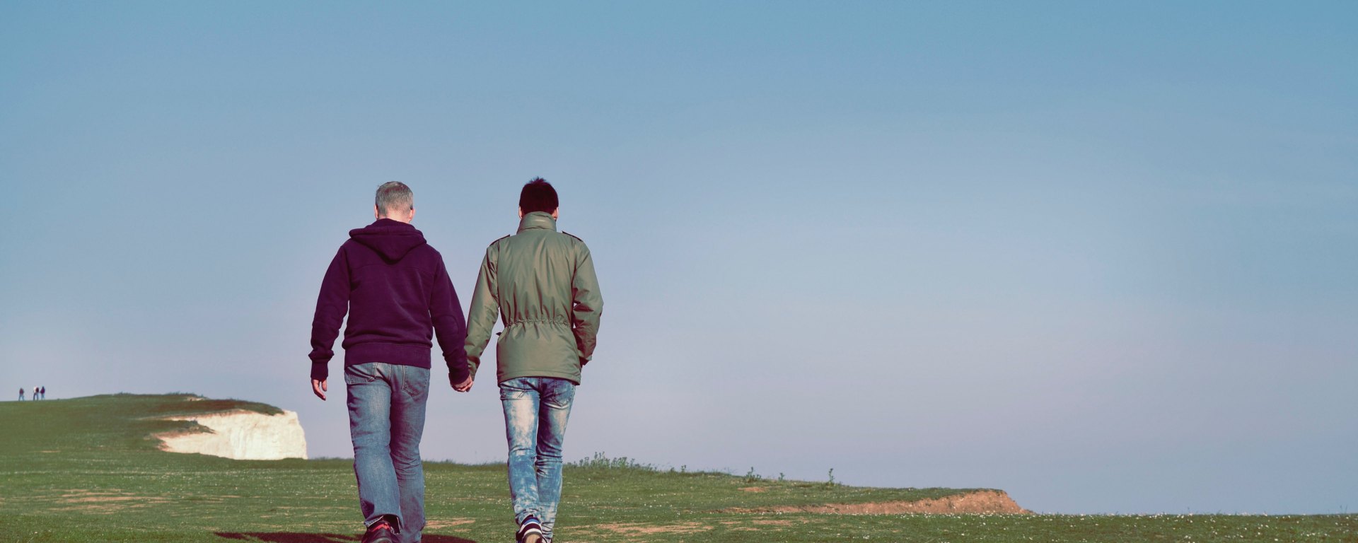 Two men walk along a cliff side, and hold hands