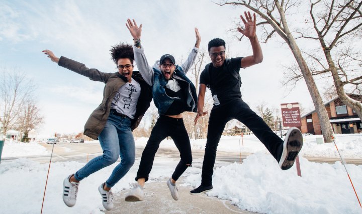 Three young people jump and laugh with their arms up