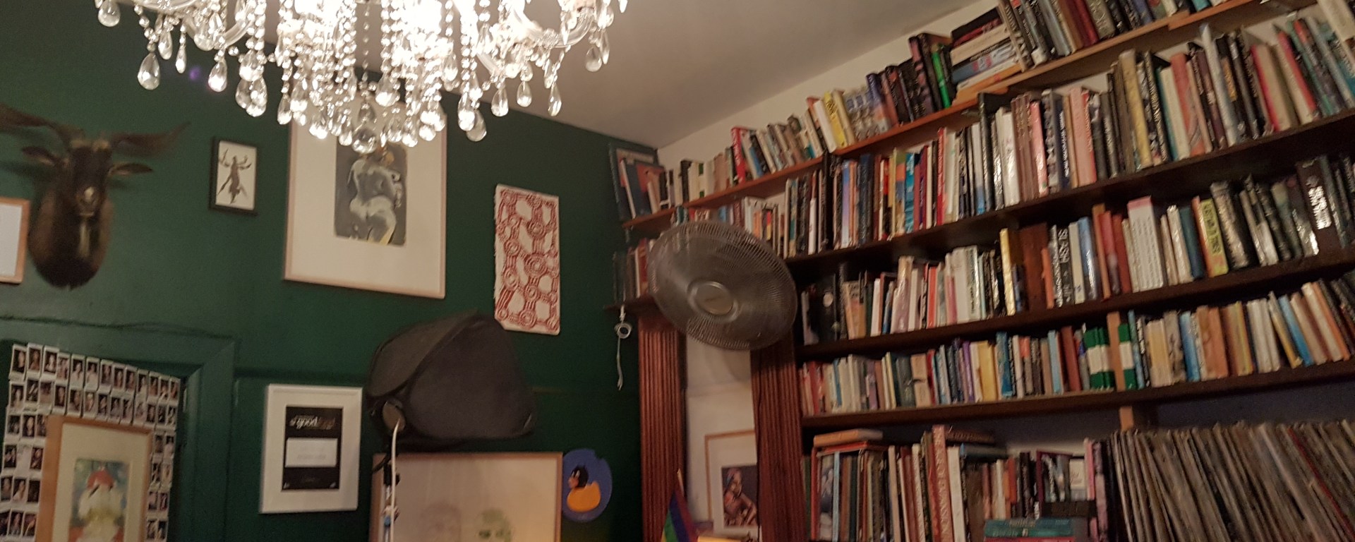 A room with a chandelier, green walls on the left, books lining the background and lots of knick knacks