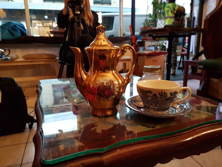 A tea pot and ornate cup on a glass top table
