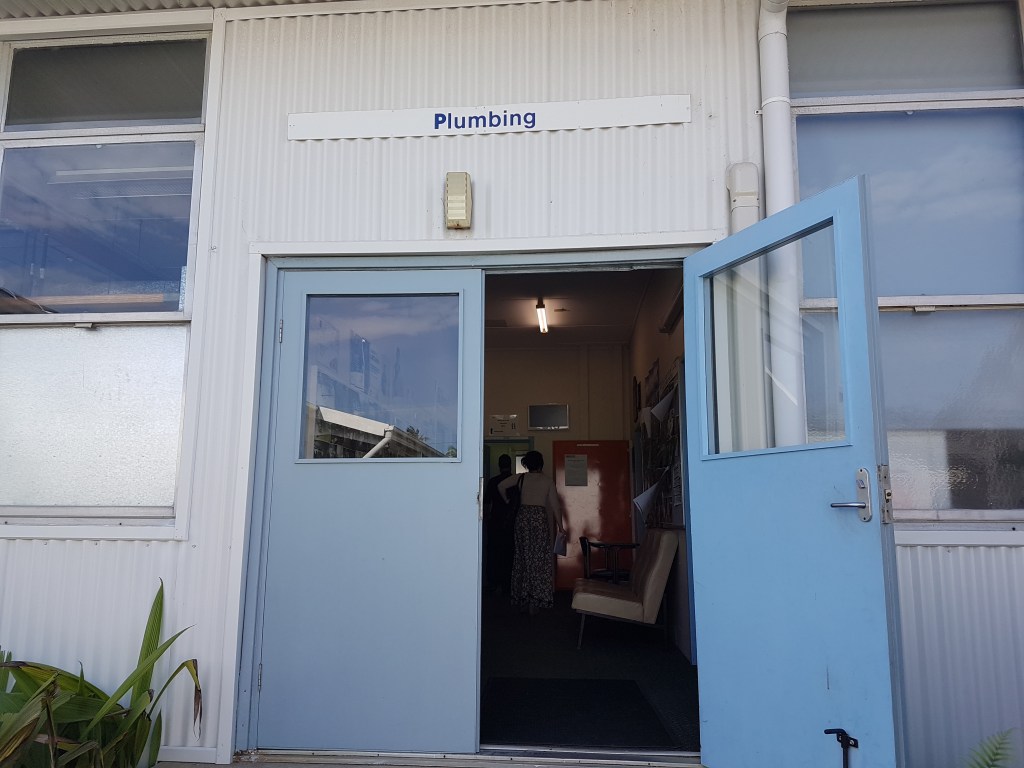 The outside of a workshop, with a sign that reads, "Plumbing"