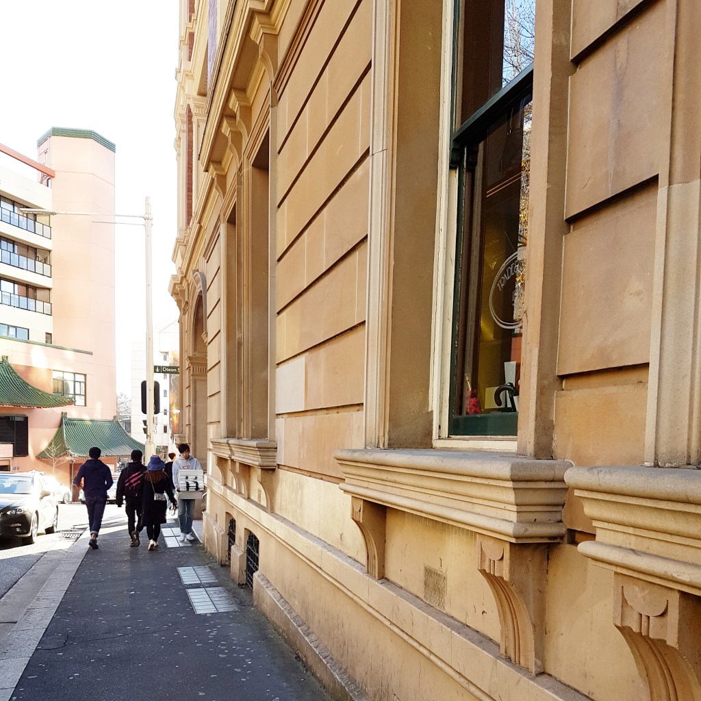 People walk down the street beside a tall building in Sydney