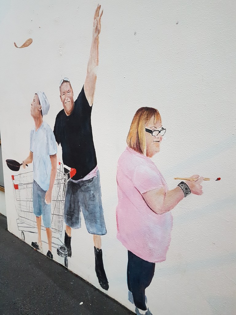 Street art outside a community organisation, showing people with disability shopping and holding up their arms happily