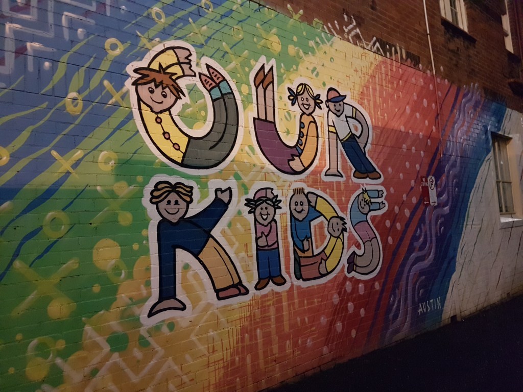 Street art outside a community organisation, showing children bending to spell out the words: Our kids
