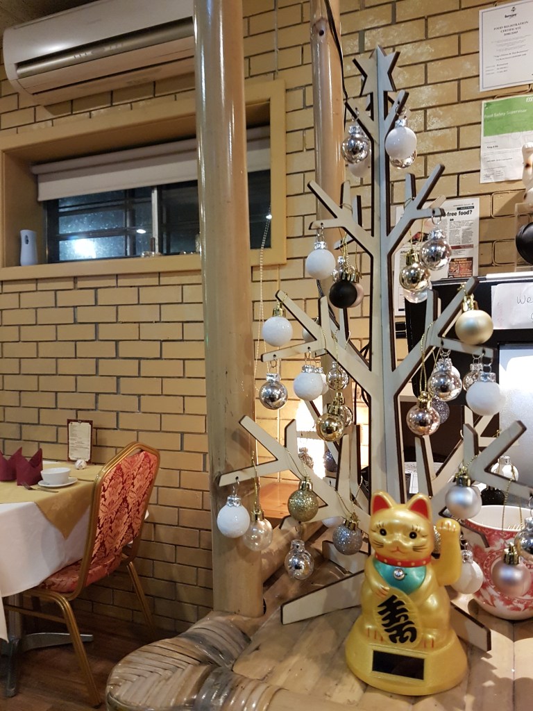 A maneki-neko statue (a lucky cat waving) underneath a wooden tree, inside a Chinese restaurant