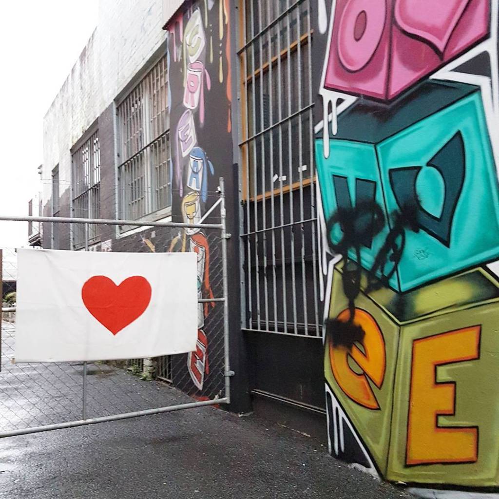Street art outside a shop that reads "Love," plus a white flag with a red love heart hanging over a gate