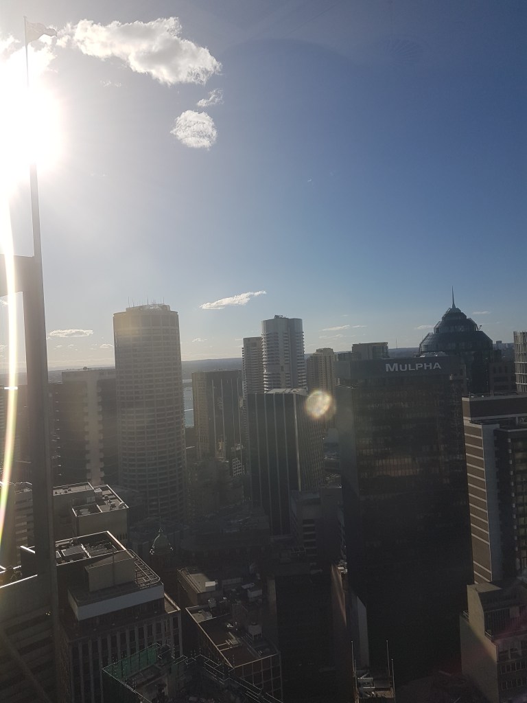 Aerial view of Sydney's central business district. There are tall buildings and rooftops, with the nearest sign saying "Mulpha"