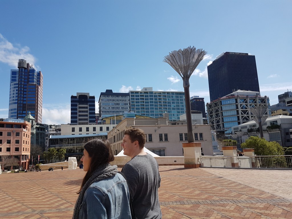 People walk outdoors, with a large sculpture in the background