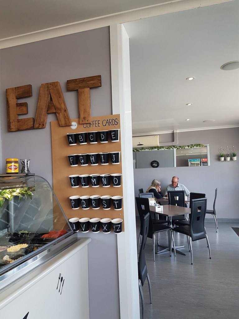 People chat inside of a cafe. There is a sign that says "EAT" across the top