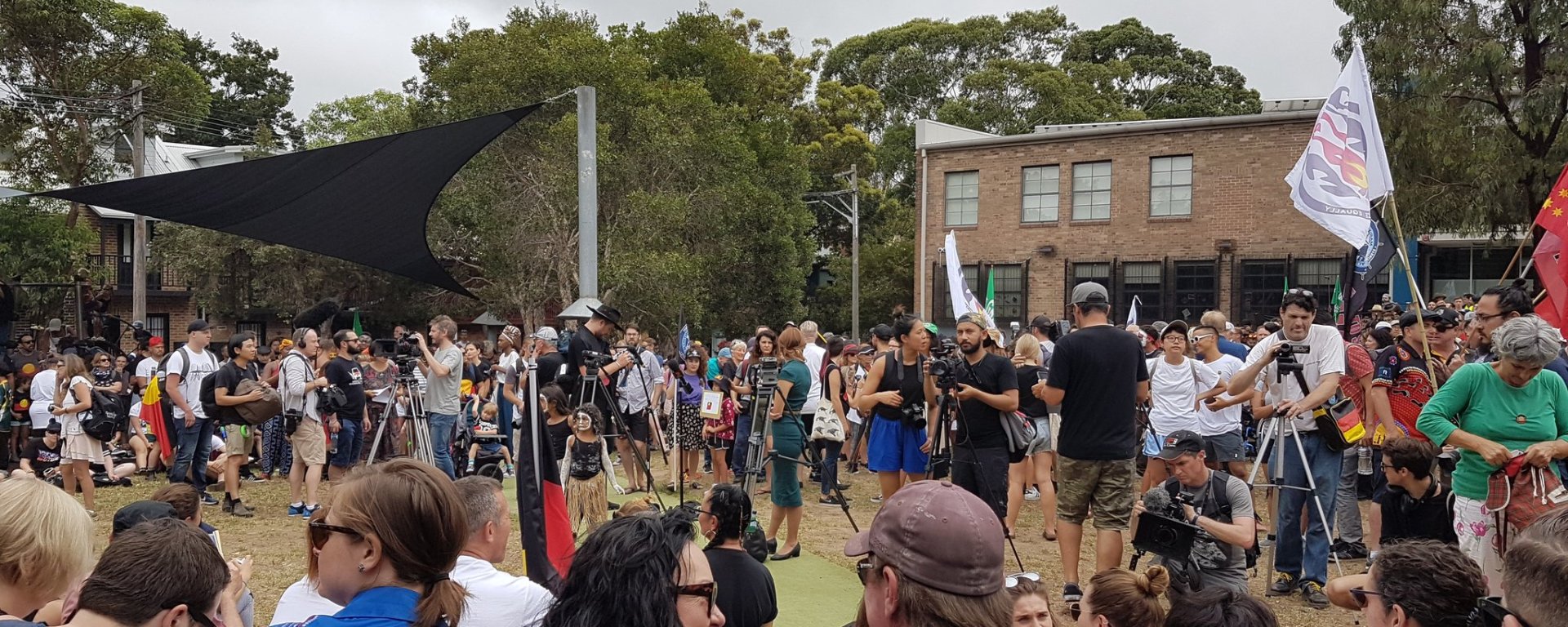 People wearing Aboriginal tshirts sit and watch protesters at the Invasion Day Protest in Redfern, Sydney