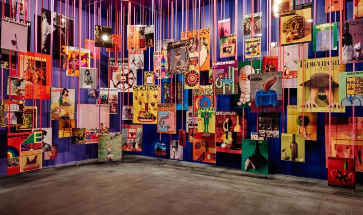A large room showing Les Mason exhibtion, or colourful posters hanging from large strings