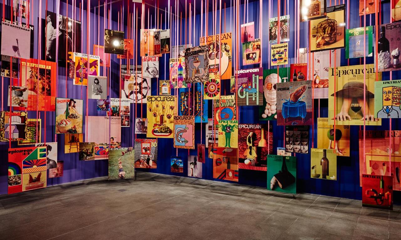 A large room showing Les Mason exhibtion, or colourful posters hanging from large strings