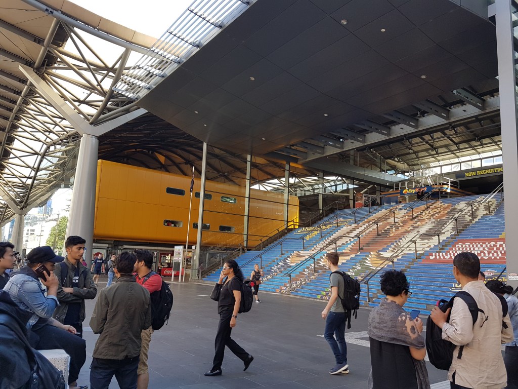 People walk outside of Southern Cross Station. There is a colourful design on the stairs