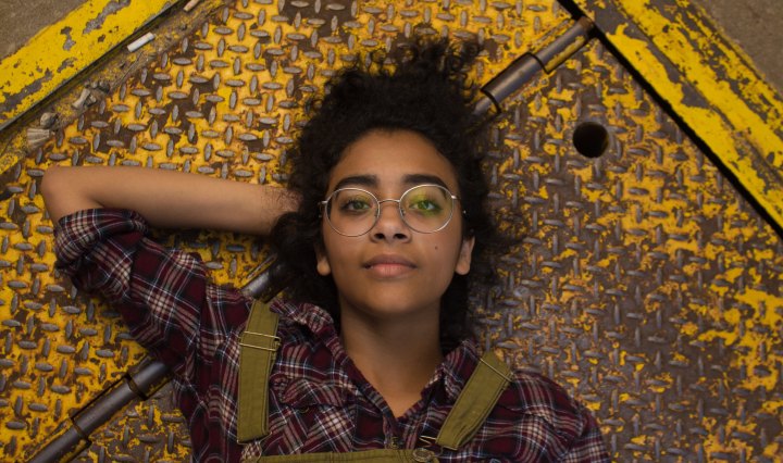 Young woman with glasses lies down on the ground with hand behind her head, looking determined