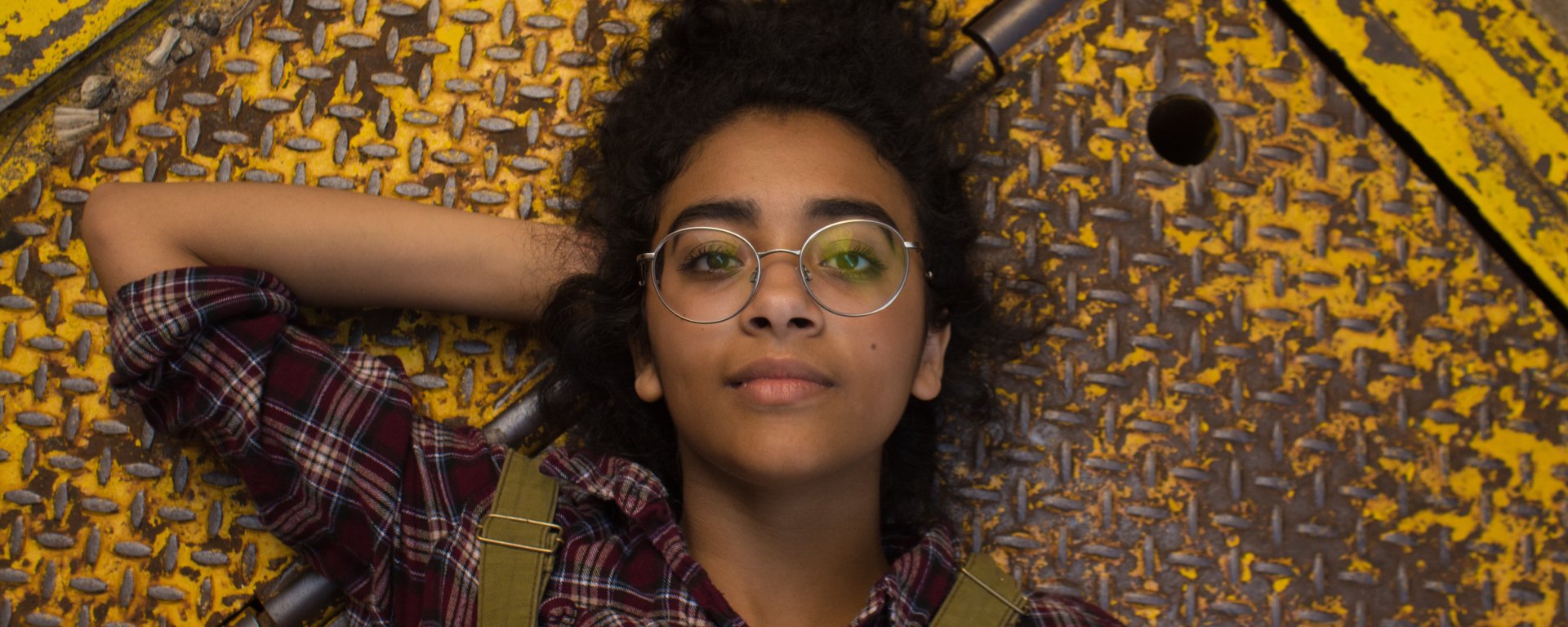 Young woman with glasses lies down on the ground with hand behind her head, looking determined