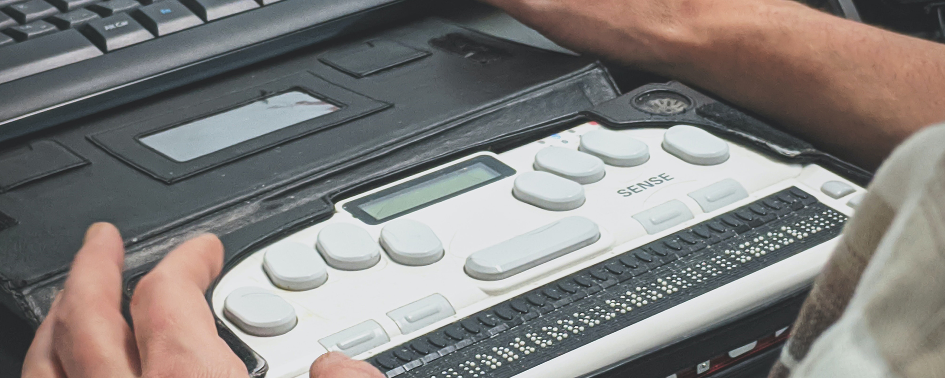 A white man's hands are seen over a braille keyboard