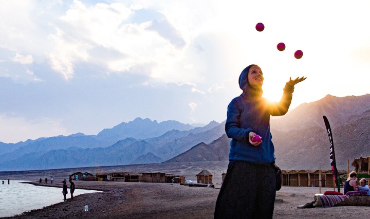 A girl if juggling on a beach wearing a hoodie