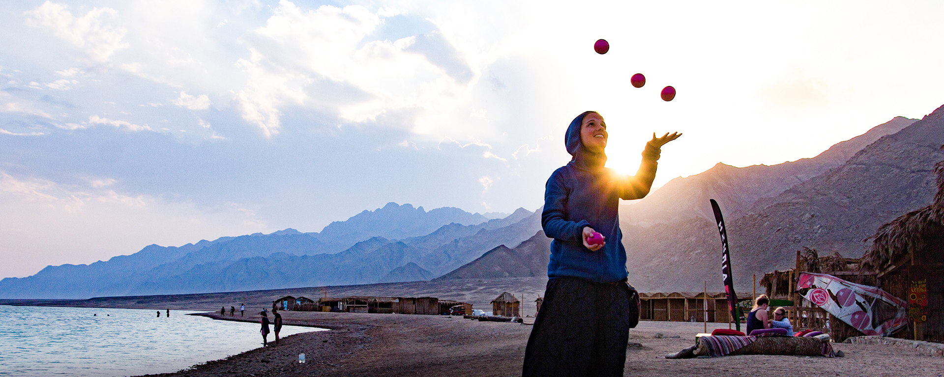 A girl if juggling on a beach wearing a hoodie