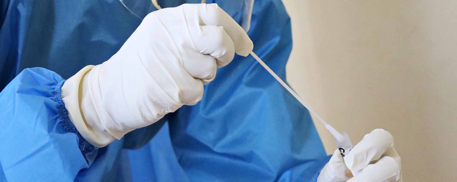 Close up of clinician's gloved hands doing a COVID-19 test with a long instrument