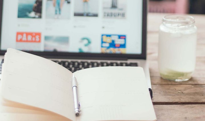 An open notebook with a laptop and glass of milk in the background