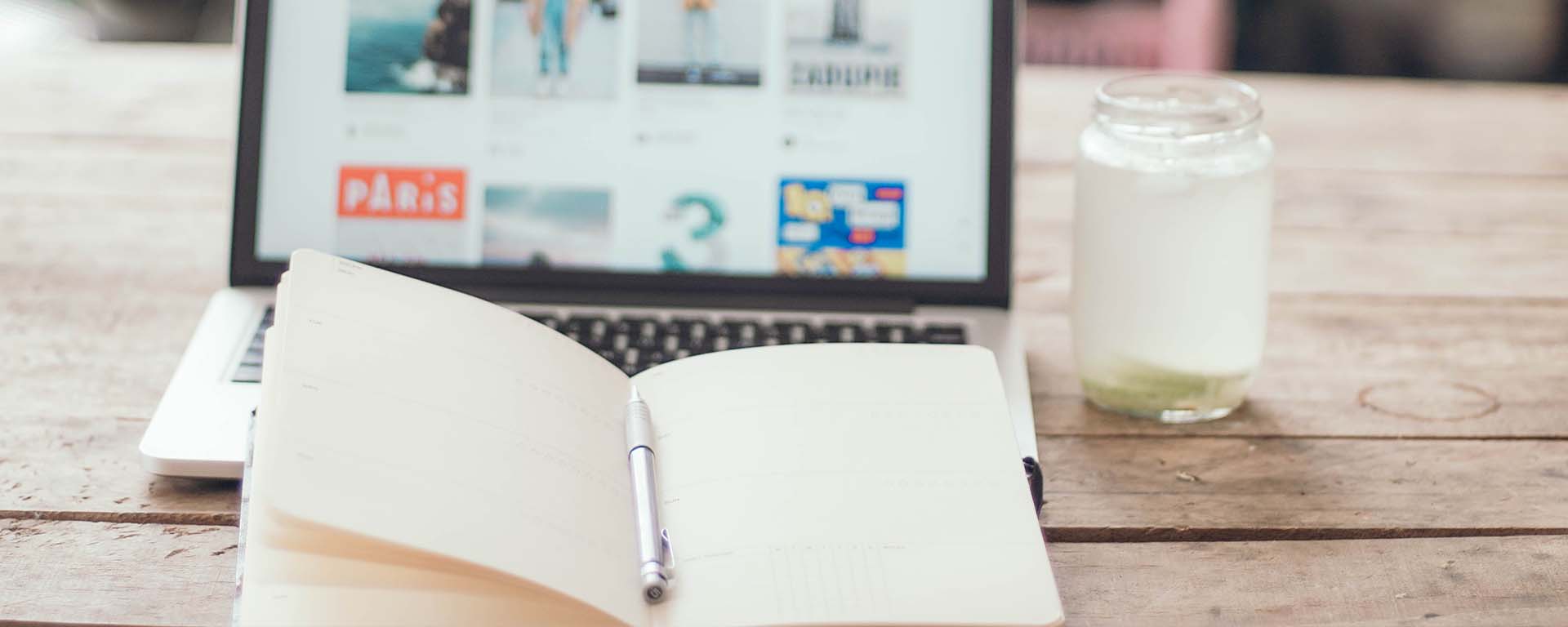 An open notebook with a laptop and glass of milk in the background