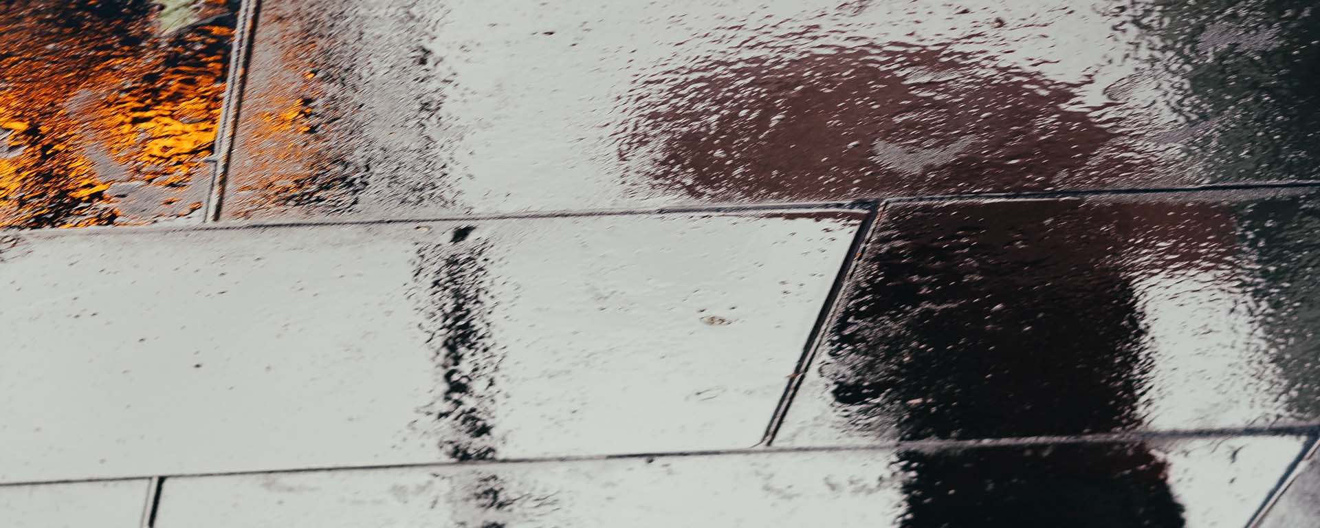 Reflection on a rainy footpath, of a person standing with an umbrella