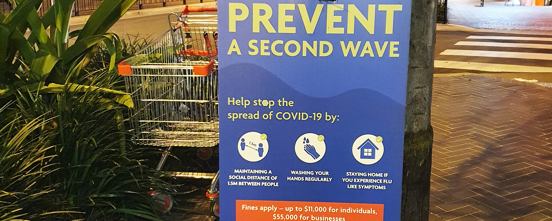 Street sign says 'Prevent aa second wave.' Next to is an abandoned shopping trolley